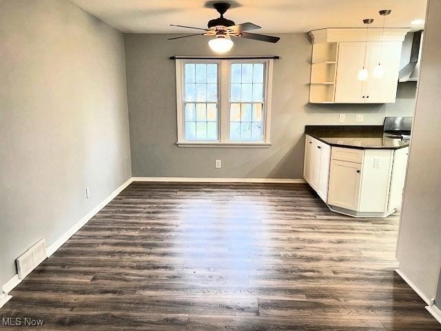 kitchen featuring pendant lighting, dark wood-type flooring, white cabinets, wall chimney exhaust hood, and ceiling fan