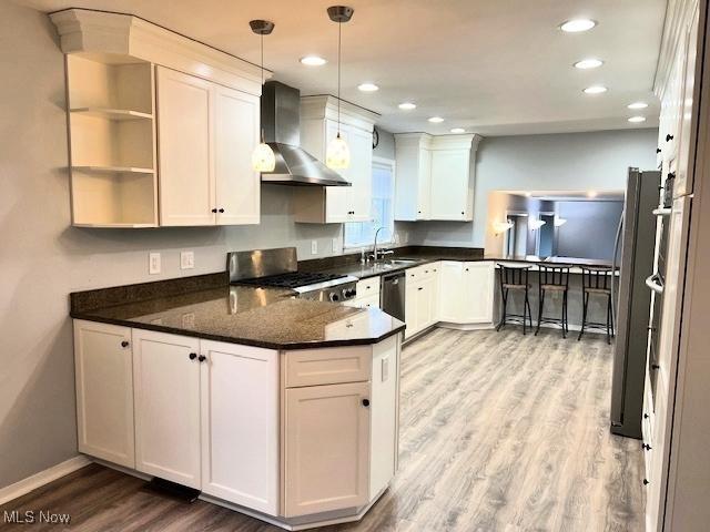 kitchen with sink, kitchen peninsula, wall chimney exhaust hood, white cabinetry, and stainless steel appliances