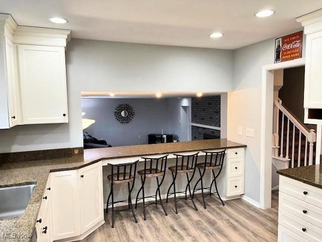 kitchen with light hardwood / wood-style floors, white cabinetry, sink, and dark stone counters