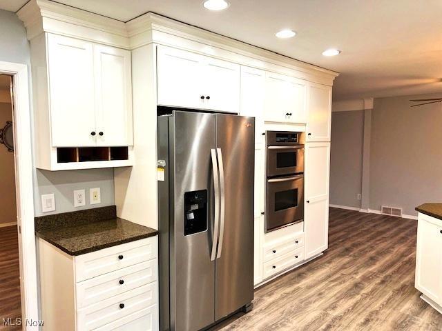 kitchen featuring dark stone counters, white cabinetry, stainless steel appliances, and hardwood / wood-style flooring