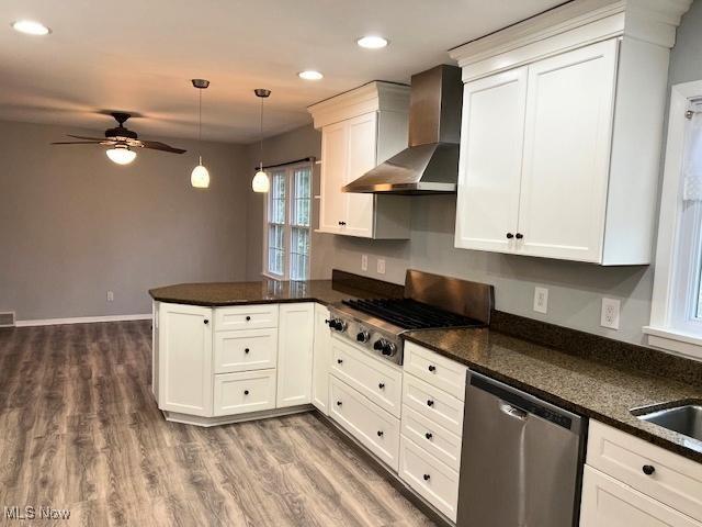 kitchen featuring kitchen peninsula, wall chimney exhaust hood, stainless steel appliances, white cabinets, and hanging light fixtures