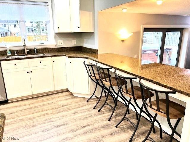 kitchen featuring sink, kitchen peninsula, dark stone countertops, light hardwood / wood-style floors, and white cabinets