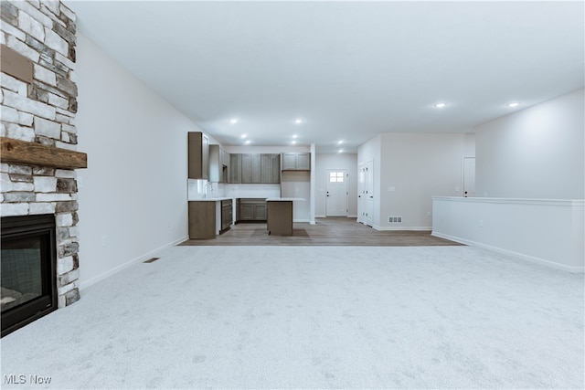 unfurnished living room with light carpet, a stone fireplace, and sink