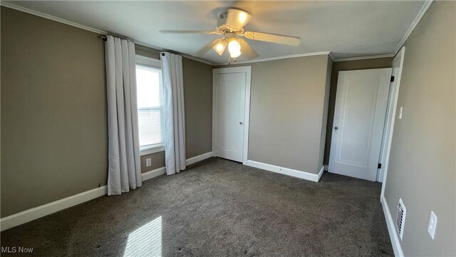 unfurnished bedroom with ornamental molding, dark colored carpet, a closet, and ceiling fan