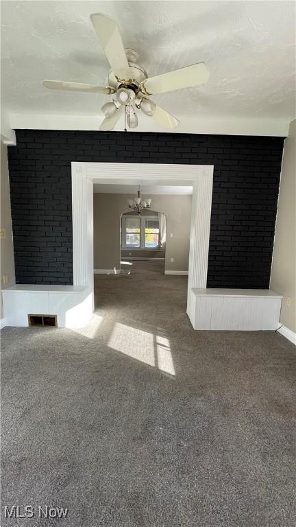 unfurnished living room featuring brick wall, a textured ceiling, carpet floors, and ceiling fan with notable chandelier