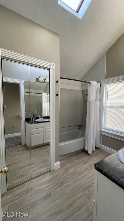 bathroom with vanity, vaulted ceiling with skylight, shower / tub combo with curtain, and wood-type flooring