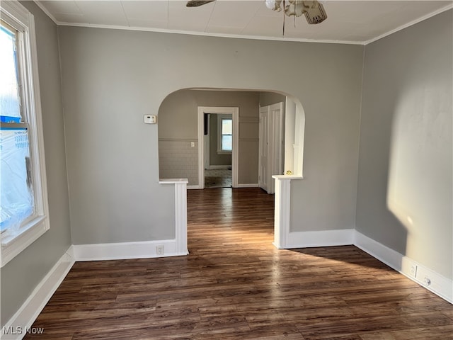 spare room with arched walkways, crown molding, baseboards, and wood finished floors