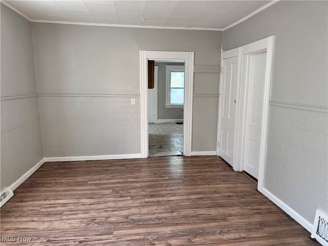 empty room with dark hardwood / wood-style flooring, ornamental molding, and tile walls