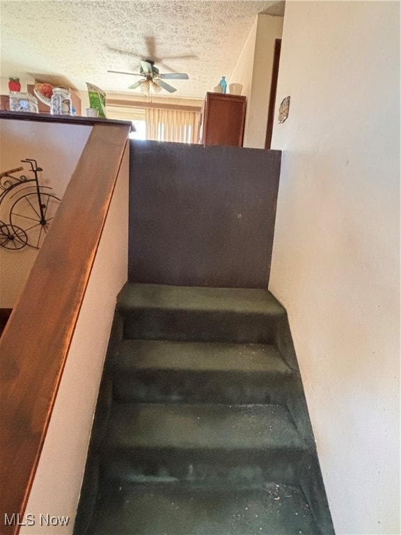 stairway with a textured ceiling and ceiling fan