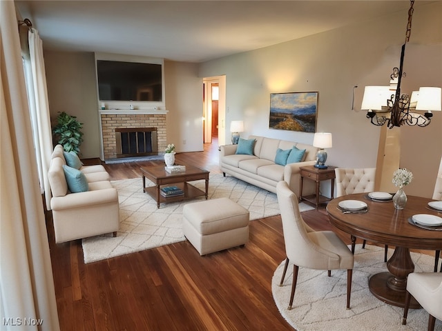 living room with a notable chandelier, hardwood / wood-style flooring, and a brick fireplace