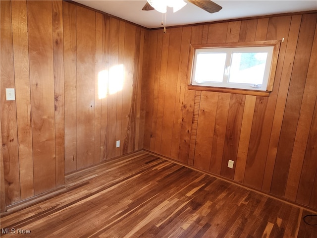 empty room featuring wood walls, dark wood-type flooring, and ceiling fan