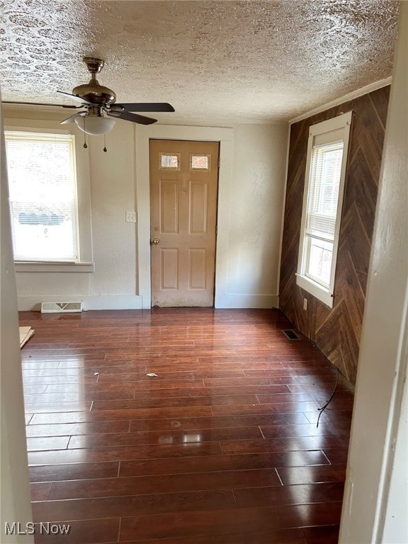 entrance foyer featuring wooden walls, dark hardwood / wood-style floors, a textured ceiling, and plenty of natural light