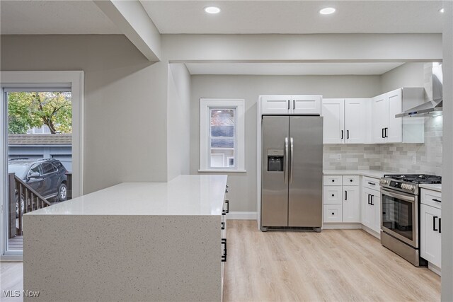 kitchen with wall chimney range hood, backsplash, light hardwood / wood-style floors, stainless steel appliances, and white cabinets