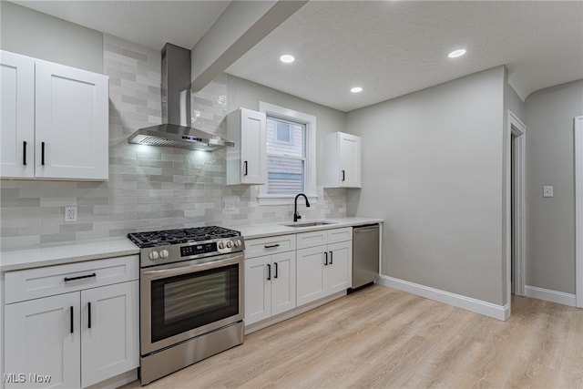 kitchen featuring appliances with stainless steel finishes, sink, light wood-type flooring, white cabinetry, and wall chimney exhaust hood