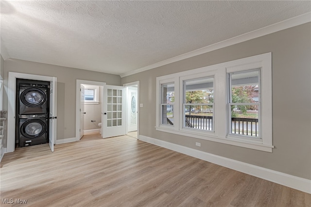 unfurnished room with light hardwood / wood-style flooring, a textured ceiling, stacked washer and dryer, and crown molding