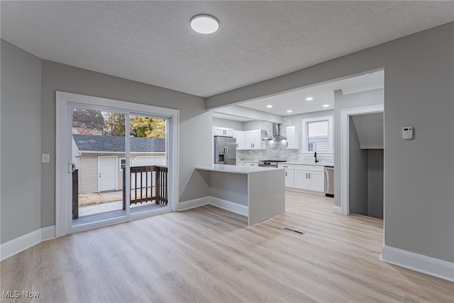 kitchen with wall chimney range hood, white cabinetry, stainless steel appliances, and plenty of natural light