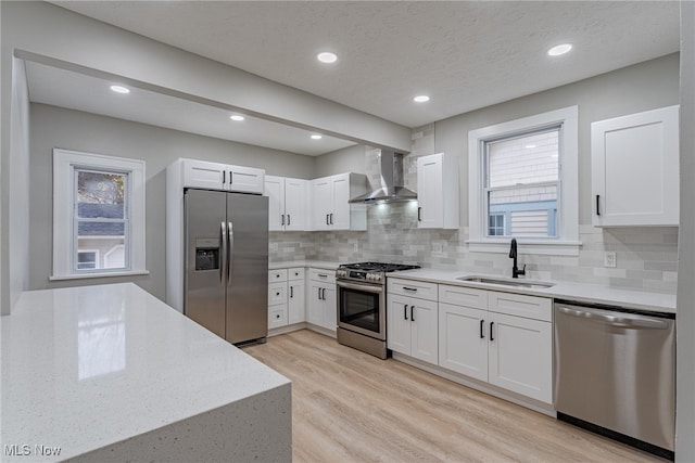 kitchen with white cabinets, appliances with stainless steel finishes, light hardwood / wood-style flooring, wall chimney exhaust hood, and sink