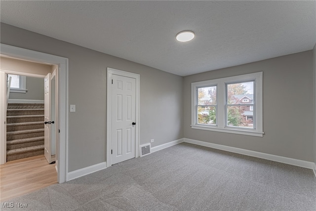 unfurnished bedroom featuring a closet, a textured ceiling, and light colored carpet