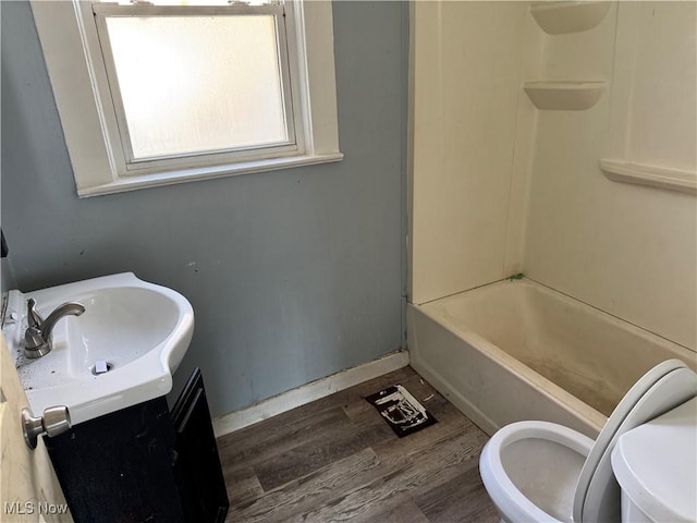 bathroom with baseboards, toilet, shower / bath combination, wood finished floors, and vanity