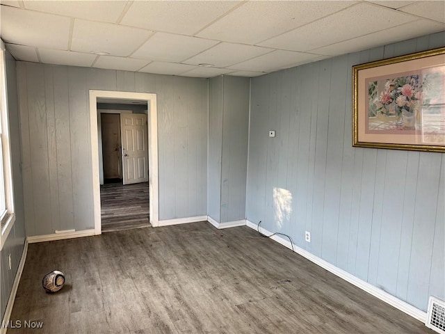 empty room featuring visible vents, wood finished floors, baseboards, and a paneled ceiling