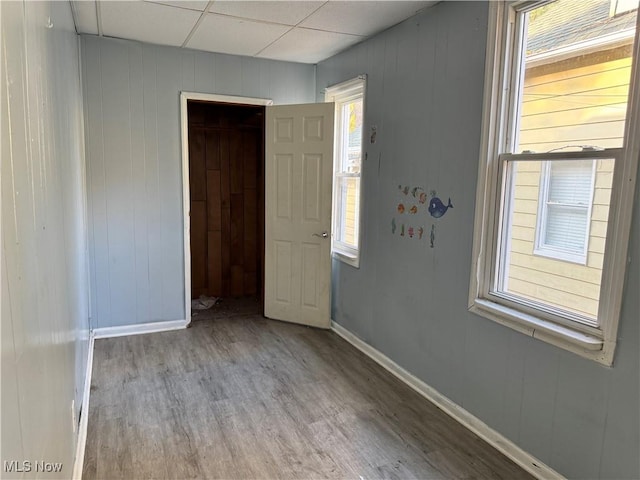 unfurnished bedroom featuring baseboards, a paneled ceiling, and wood finished floors