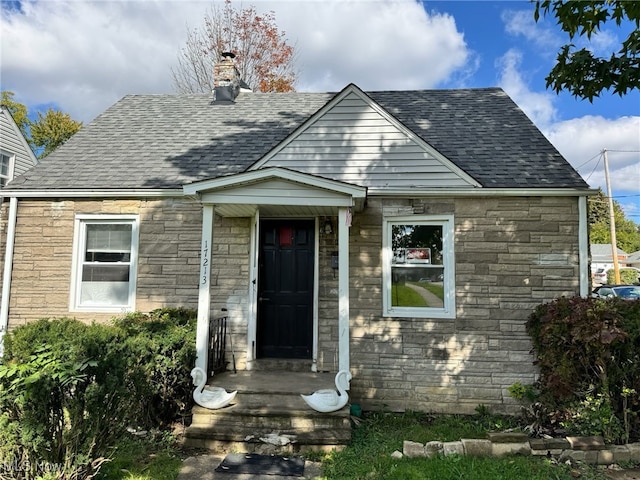 bungalow with stone siding, a chimney, and roof with shingles