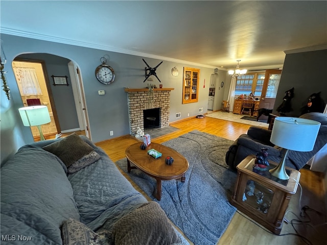 living room with crown molding, wood-type flooring, a brick fireplace, and a notable chandelier