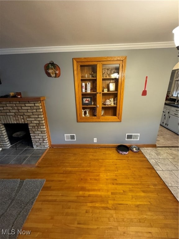 unfurnished living room featuring crown molding, a stone fireplace, and light hardwood / wood-style floors