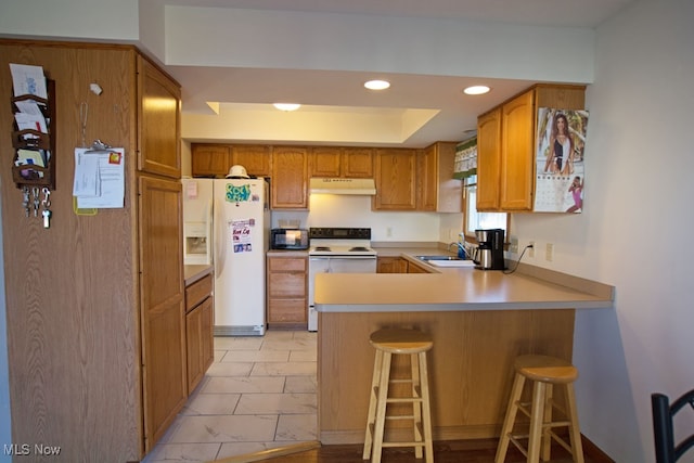 kitchen with kitchen peninsula, sink, white appliances, and a breakfast bar area