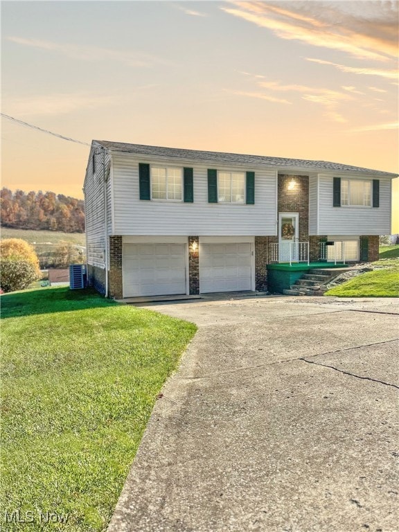 bi-level home with central air condition unit, a yard, and a garage