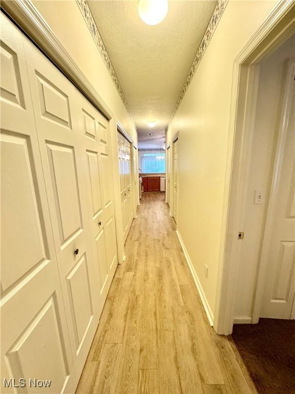 hall with a textured ceiling, light wood-style flooring, and baseboards