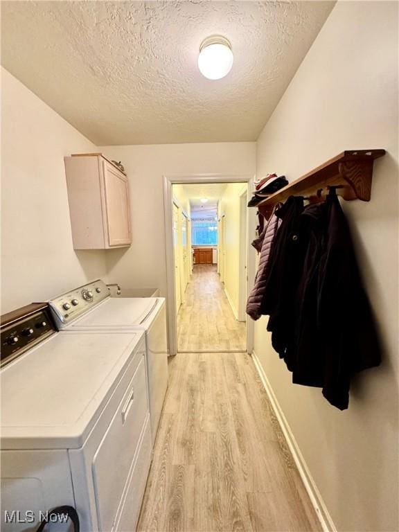 washroom with a textured ceiling, light wood-style flooring, baseboards, washer and dryer, and cabinet space