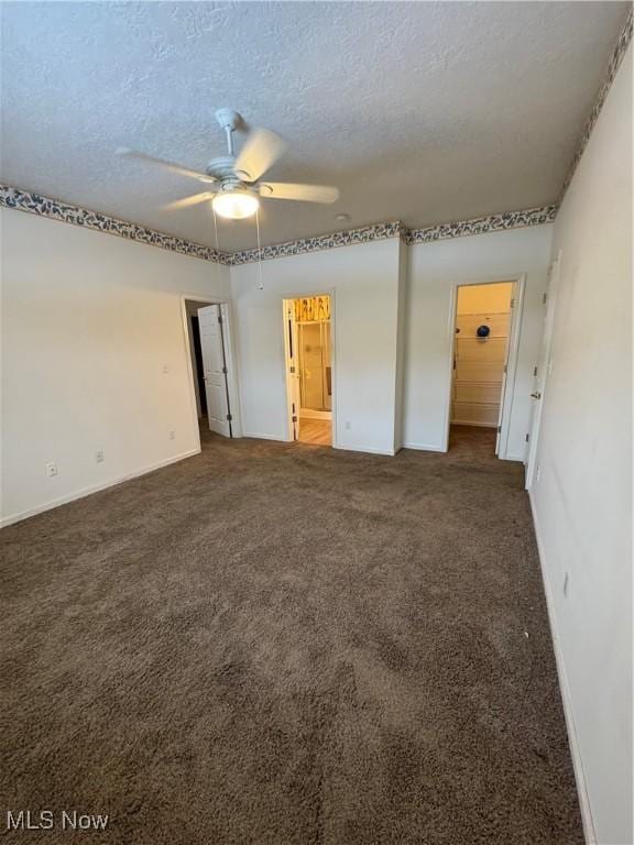 empty room featuring a textured ceiling, dark colored carpet, a ceiling fan, and baseboards