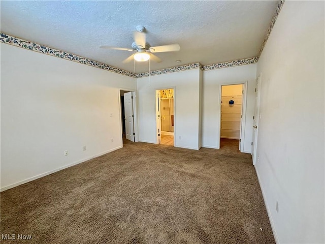 unfurnished bedroom with baseboards, ensuite bath, a walk in closet, a textured ceiling, and carpet floors