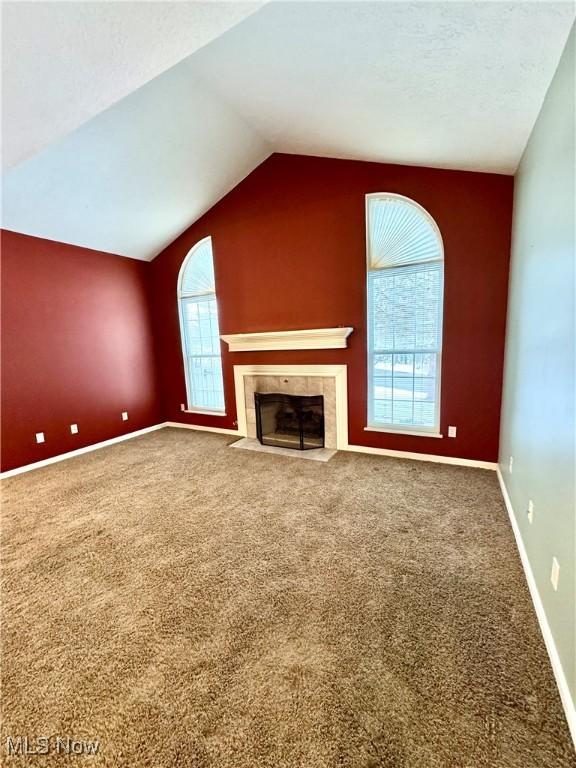 unfurnished living room featuring baseboards, a tile fireplace, vaulted ceiling, a textured ceiling, and carpet floors