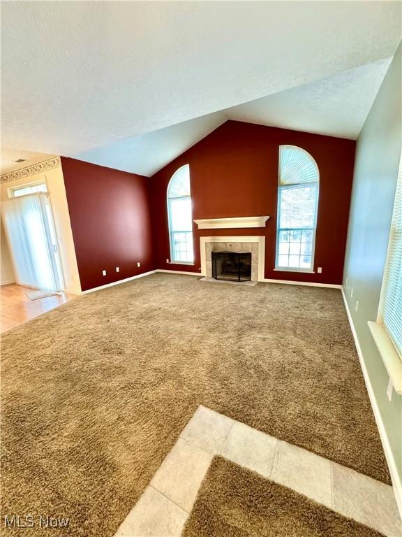 unfurnished living room with lofted ceiling, a fireplace, baseboards, and carpet flooring