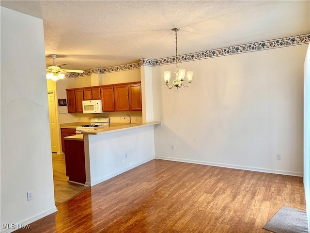 kitchen with range, brown cabinetry, white microwave, light countertops, and pendant lighting