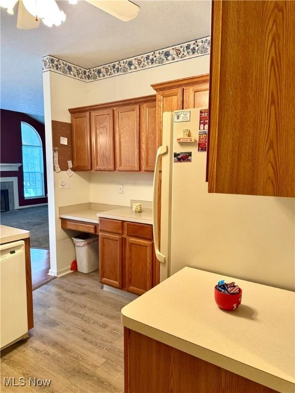 kitchen featuring white appliances, a tiled fireplace, light wood-style flooring, brown cabinets, and light countertops