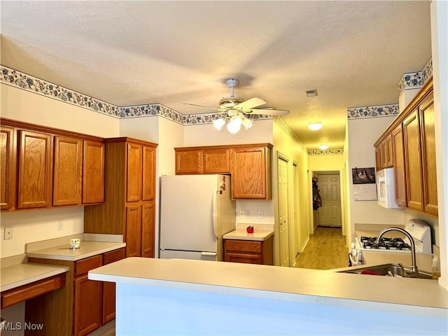 kitchen with a peninsula, white appliances, visible vents, light countertops, and brown cabinetry