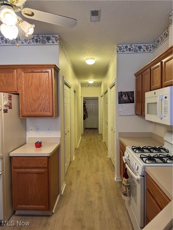 kitchen with white appliances, visible vents, brown cabinetry, light countertops, and light wood-style floors