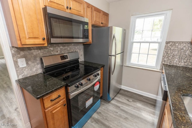 kitchen with stainless steel appliances, dark stone countertops, light wood-type flooring, and tasteful backsplash