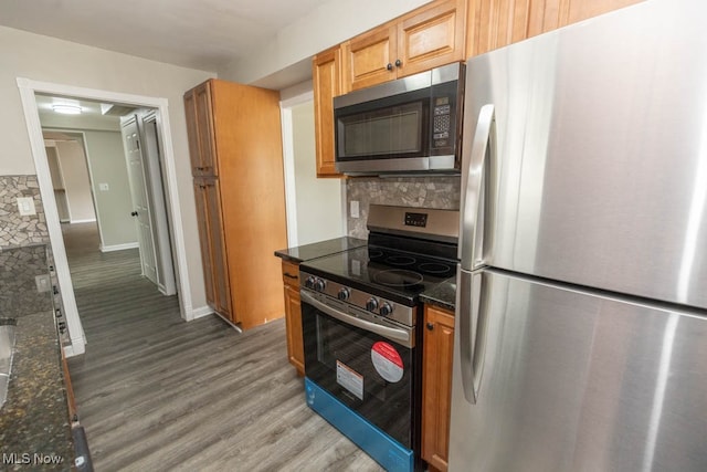 kitchen with decorative backsplash, appliances with stainless steel finishes, wood-type flooring, and dark stone counters