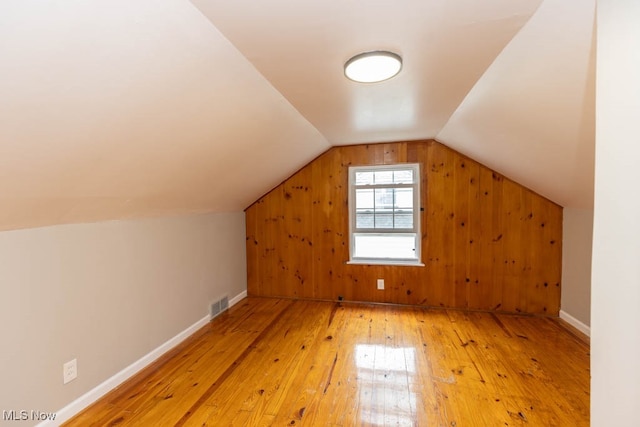 additional living space with wood walls, lofted ceiling, and hardwood / wood-style floors