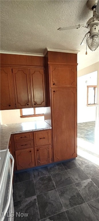 kitchen with a textured ceiling, dark tile patterned flooring, range, and crown molding