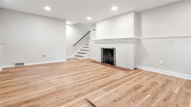 unfurnished living room featuring light wood-type flooring and a brick fireplace