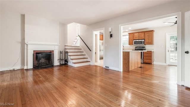 unfurnished living room with a brick fireplace, ceiling fan, plenty of natural light, and light wood-type flooring