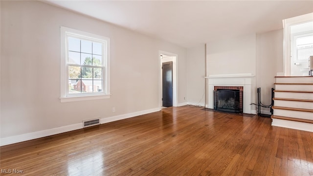 unfurnished living room featuring hardwood / wood-style floors and a brick fireplace