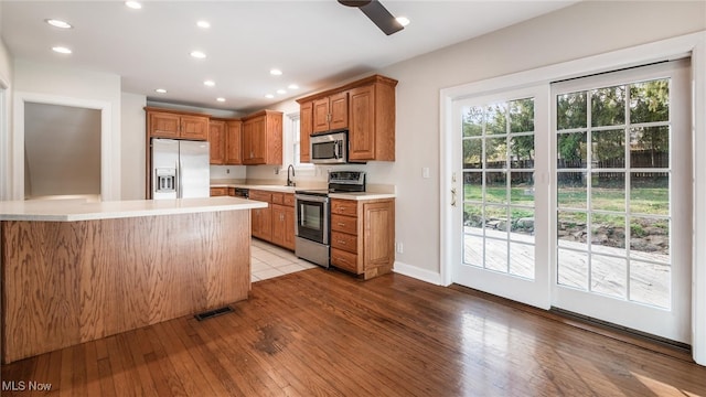 kitchen with stainless steel appliances, ceiling fan, sink, and light hardwood / wood-style flooring