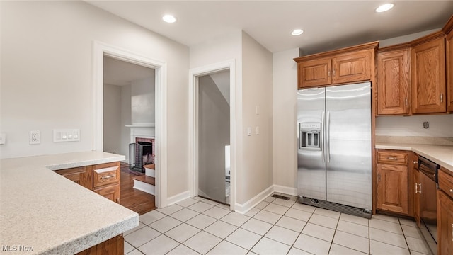 kitchen with stainless steel fridge with ice dispenser, black dishwasher, light tile patterned flooring, and a brick fireplace