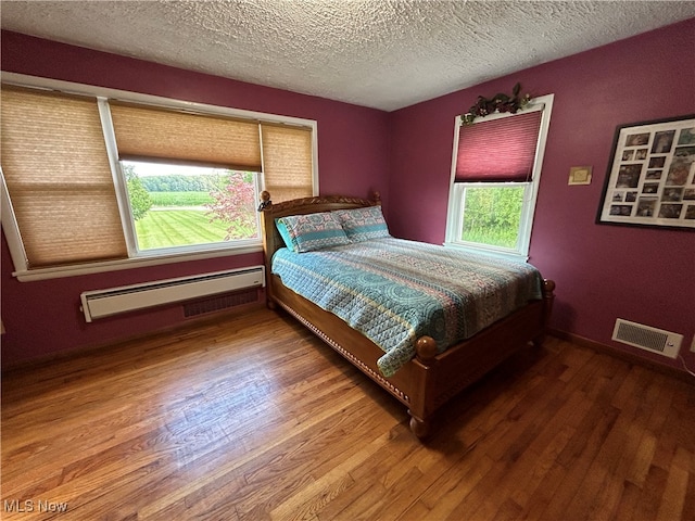 bedroom featuring a textured ceiling, wood-type flooring, and a baseboard heating unit